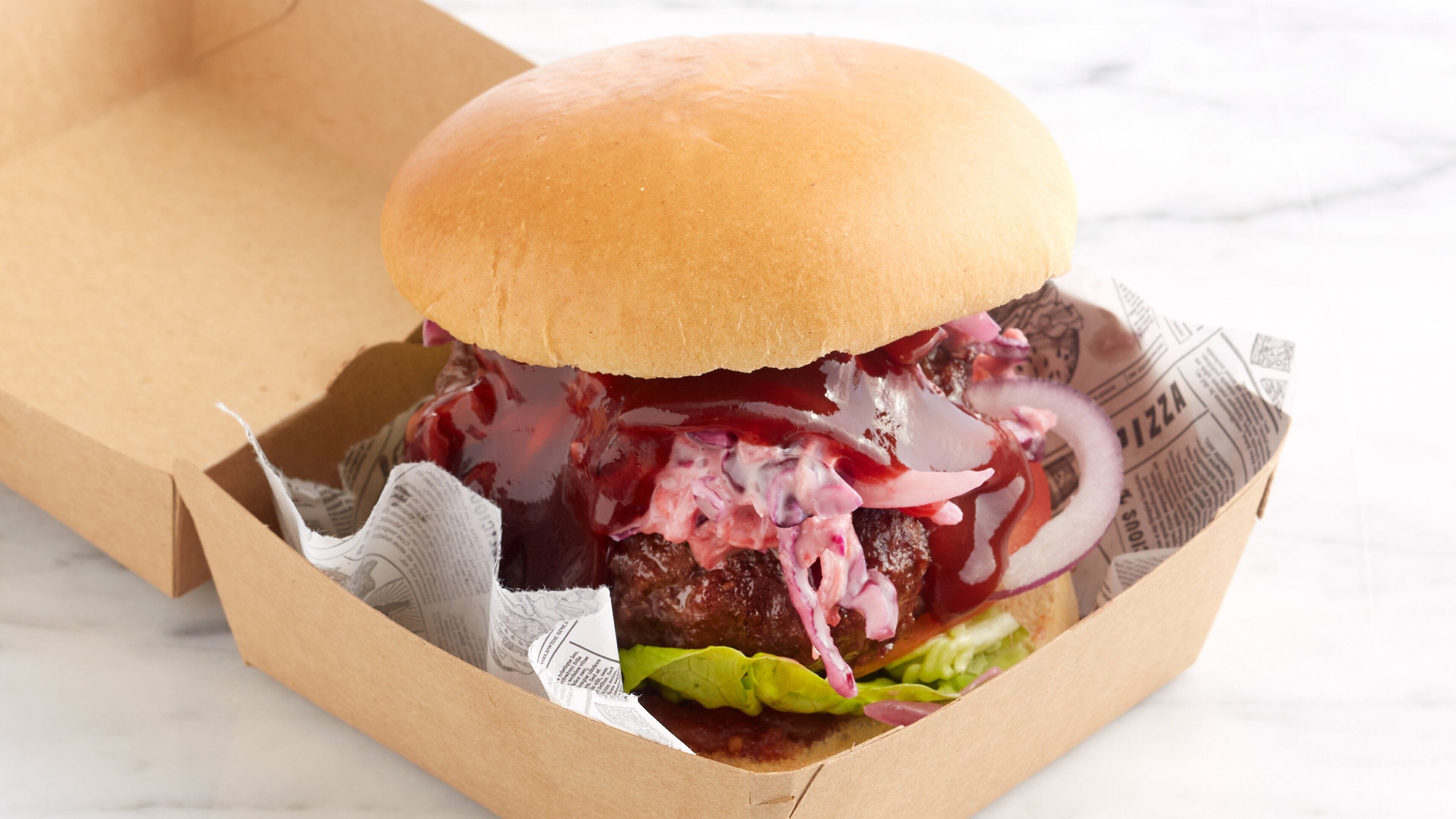 A burger in a paper container with lettuce, red onion, and a sauce.