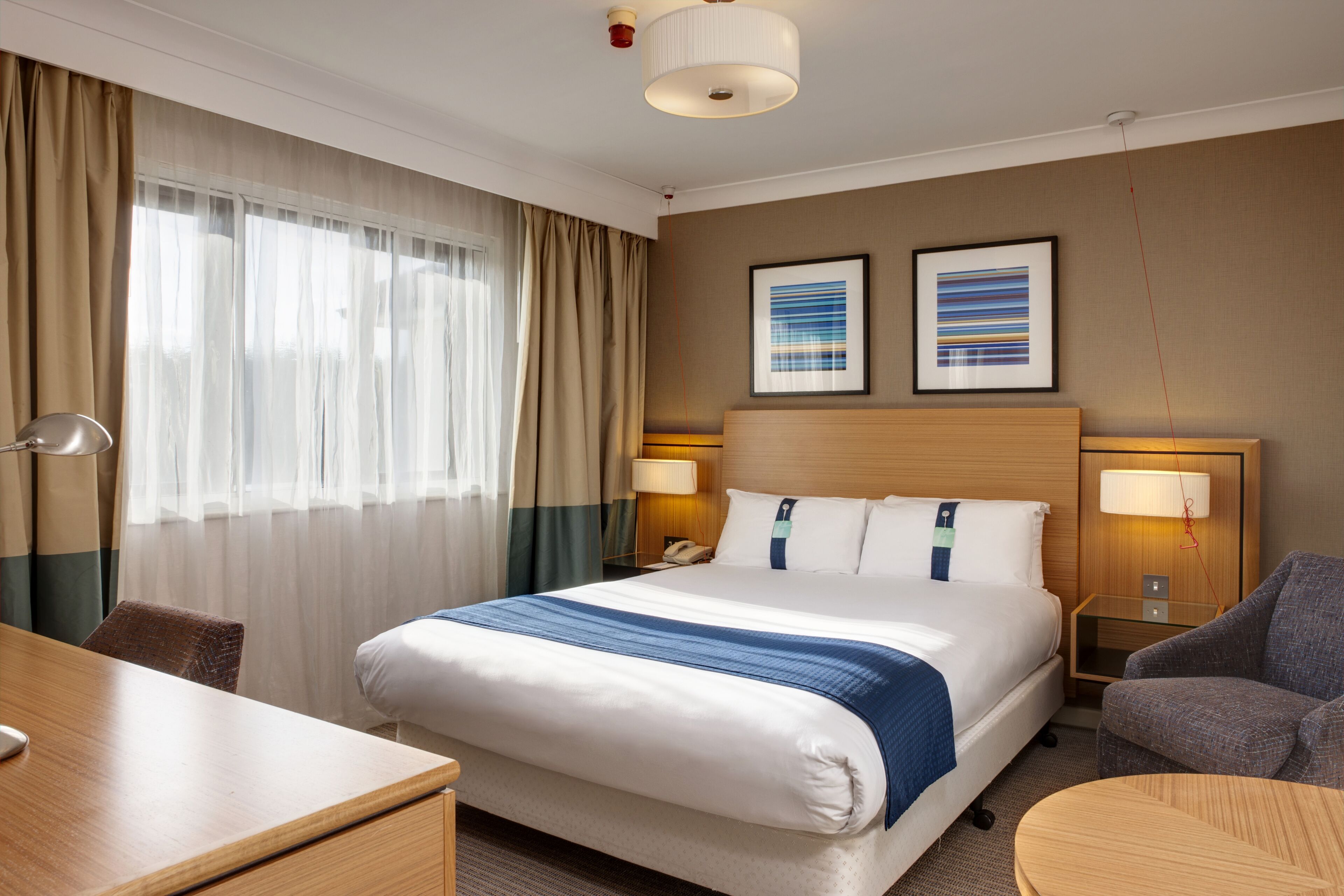 A hotel room with a large bed, two bedside tables with lamps, a desk, and a chair.