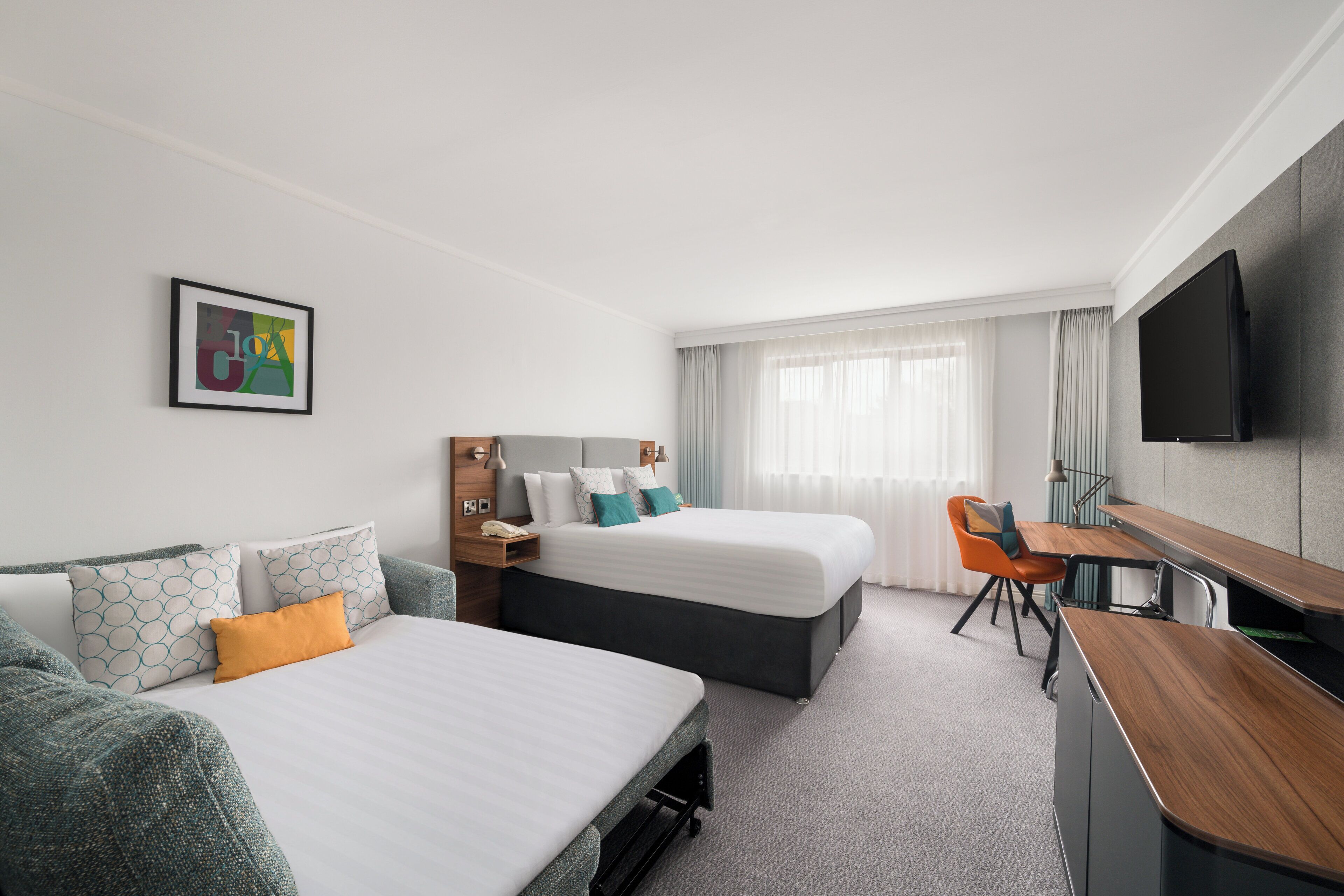 A hotel room with two beds, a desk, a TV, and a window with curtains.