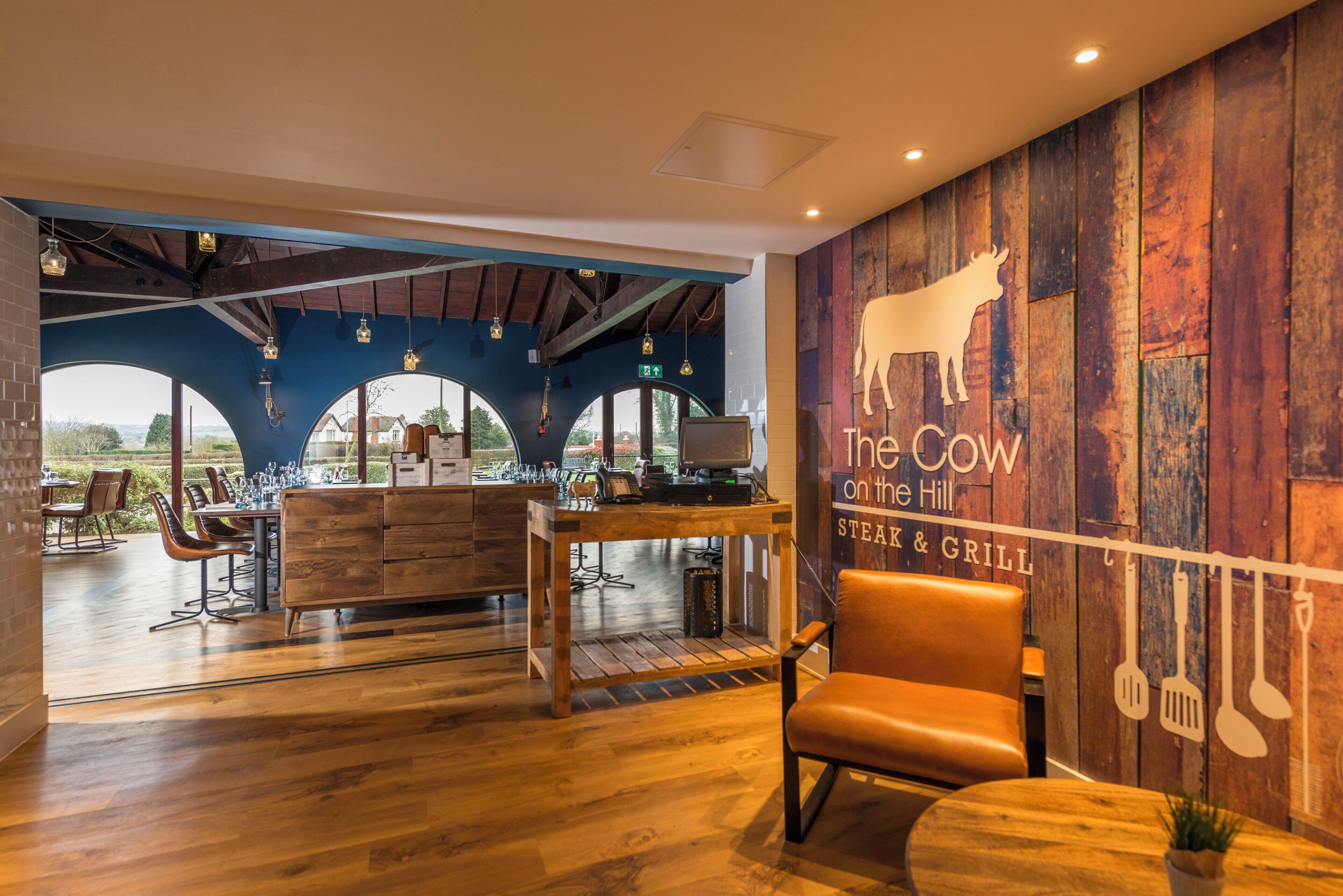 A restaurant interior with wooden flooring, a bar area, and a seating section with tables and chairs.