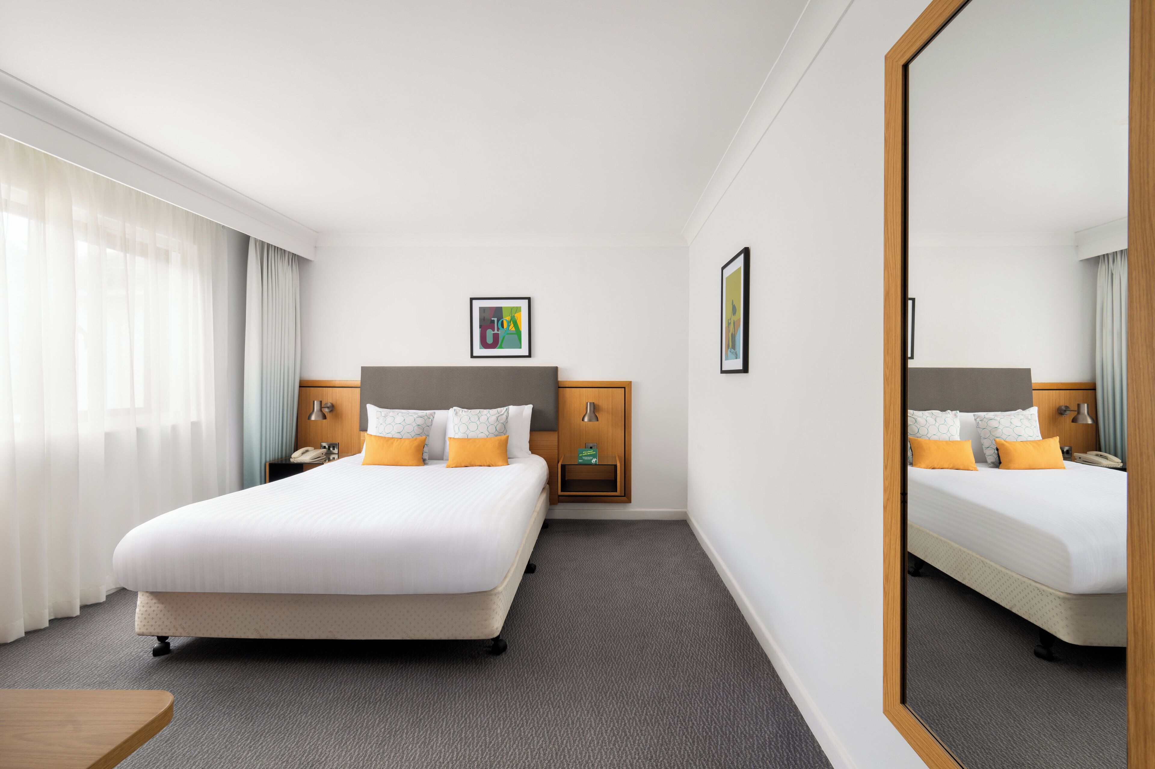 Una habitación de hotel con una cama grande, una mesita de noche, un espejo y un armario pequeño.