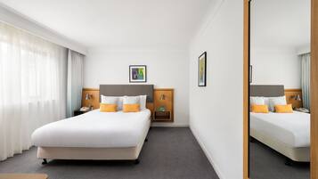 Una habitación de hotel con una cama grande, una mesita de noche, un espejo y un armario pequeño.