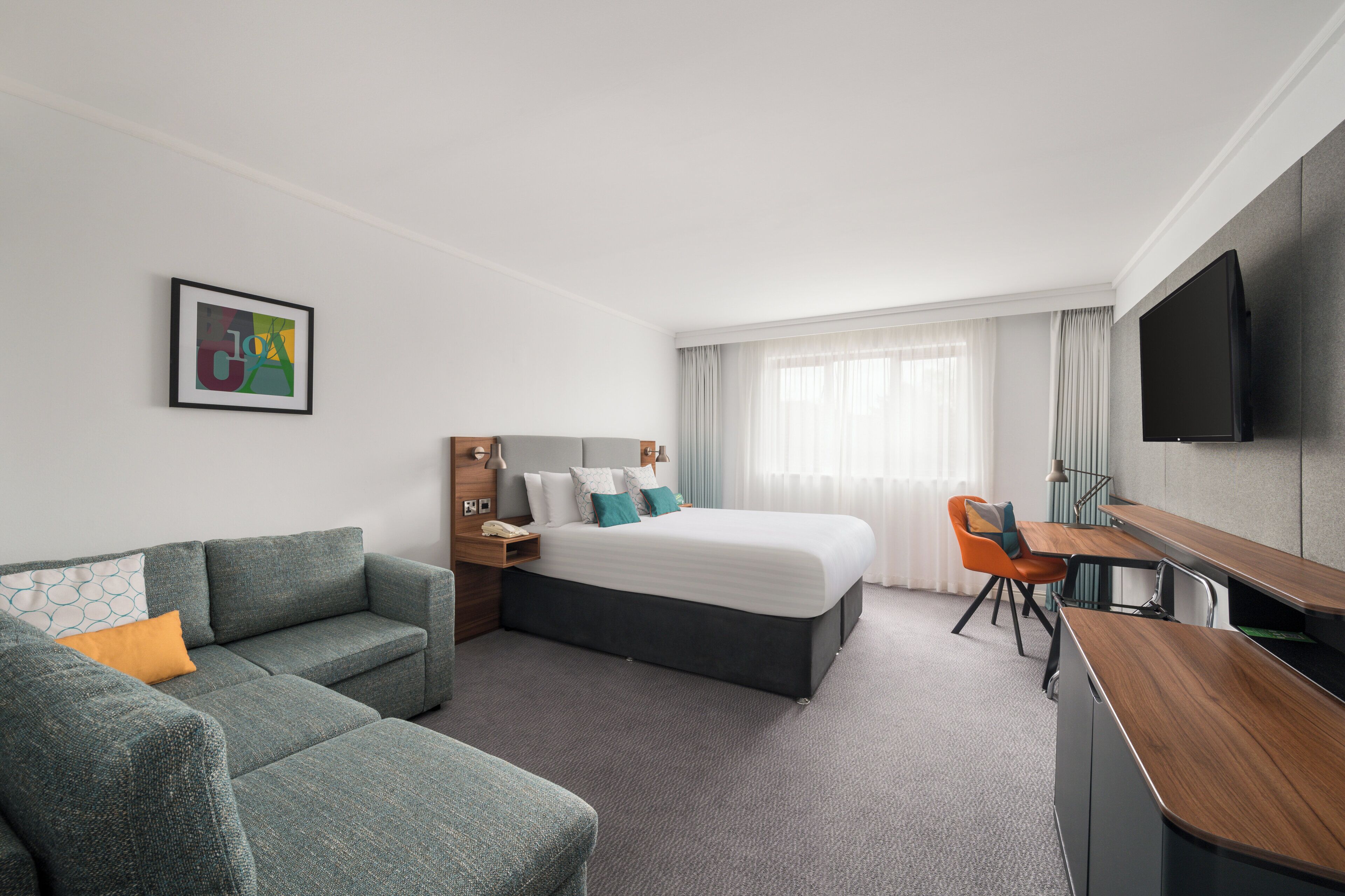 A modern hotel room with a bed, a sofa, a desk, and a TV.