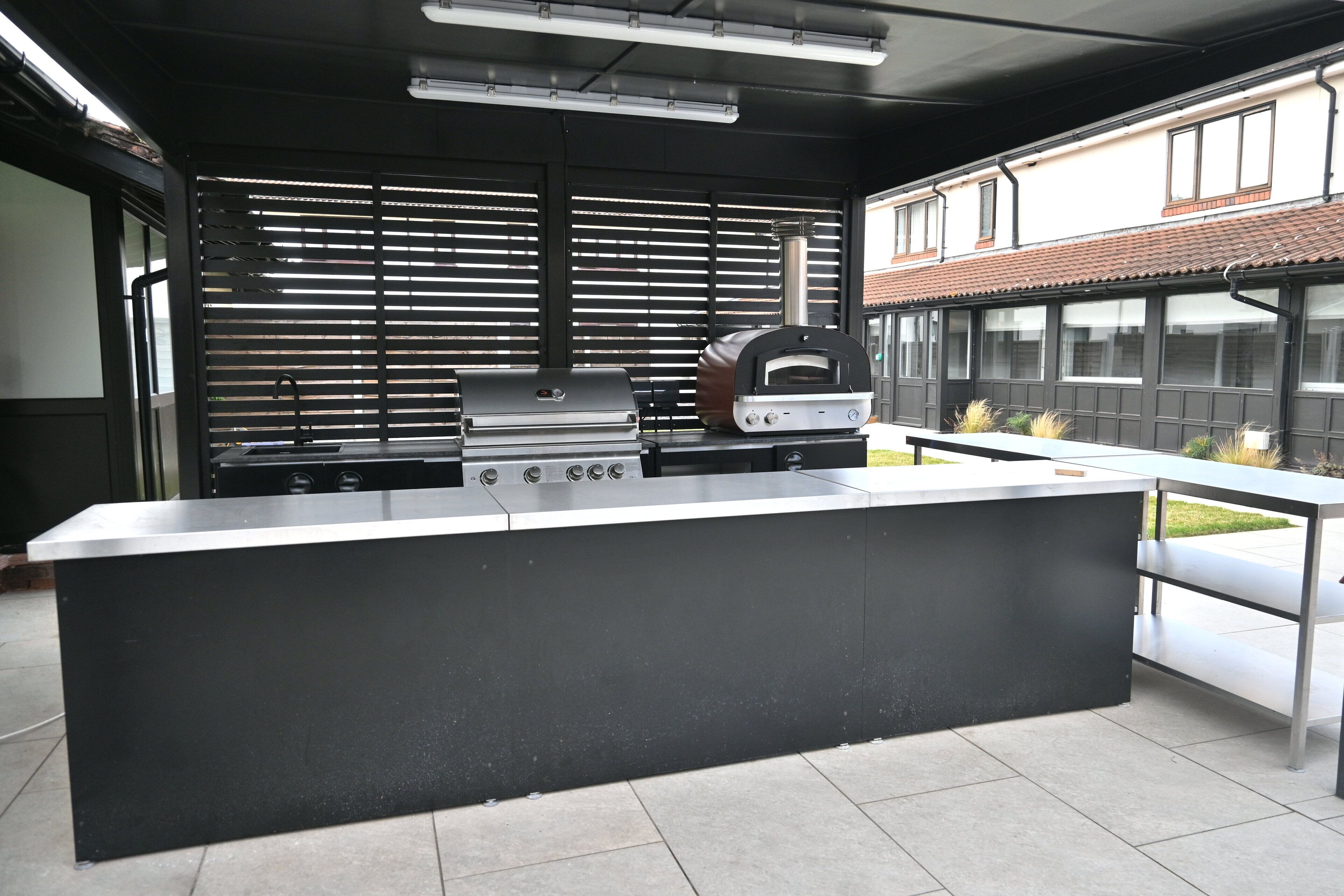 An outdoor kitchen area with a built-in grill, a pizza oven, and a stainless steel countertop.