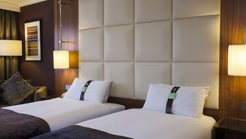 A hotel room with two beds, a large padded headboard, bedside lamps, and a framed picture on the wall.