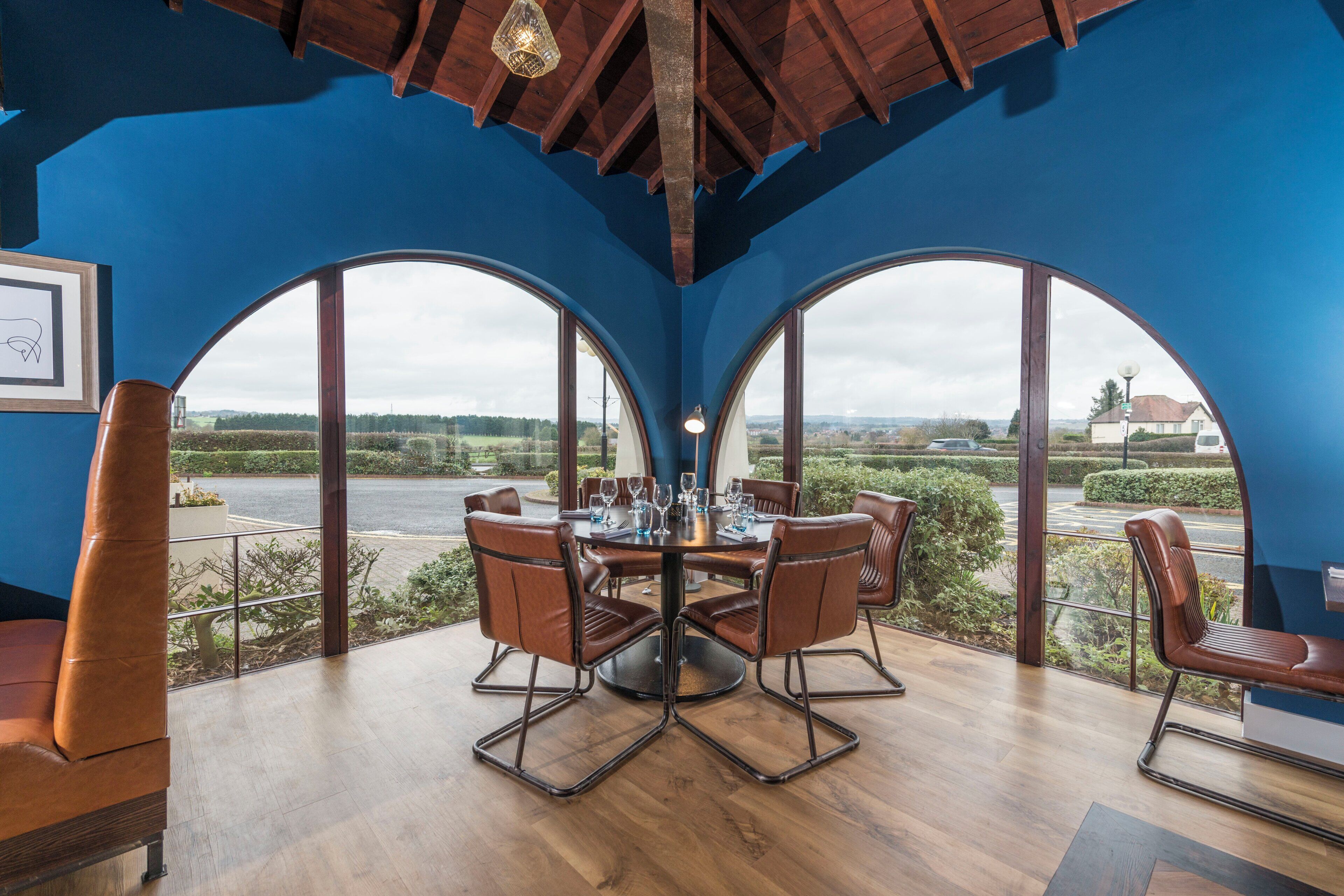 A dining area with a round table and chairs, large arched windows, and a view of the countryside.