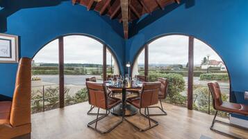 A dining area with a round table and chairs, large arched windows, and a view of the countryside.
