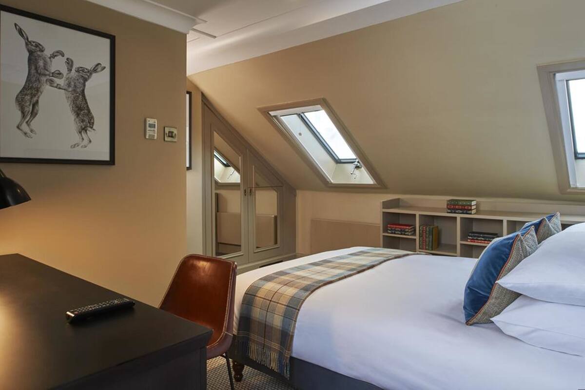 Een hotelkamer met een bed, een bureau, een stoel, een dakraam en een boekenkast.