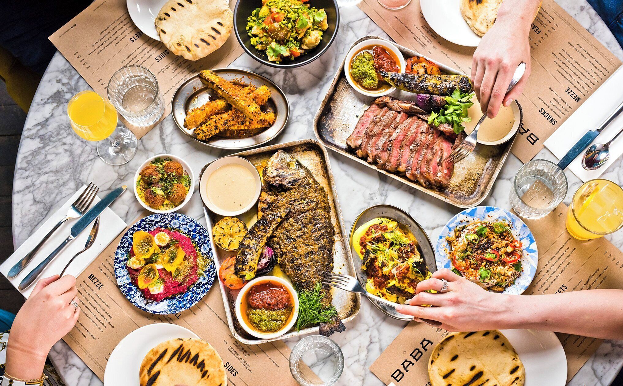 Una mesa servida con diversos platos, incluyendo carne a la parrilla, pescado y verduras, además de bebidas y pan.