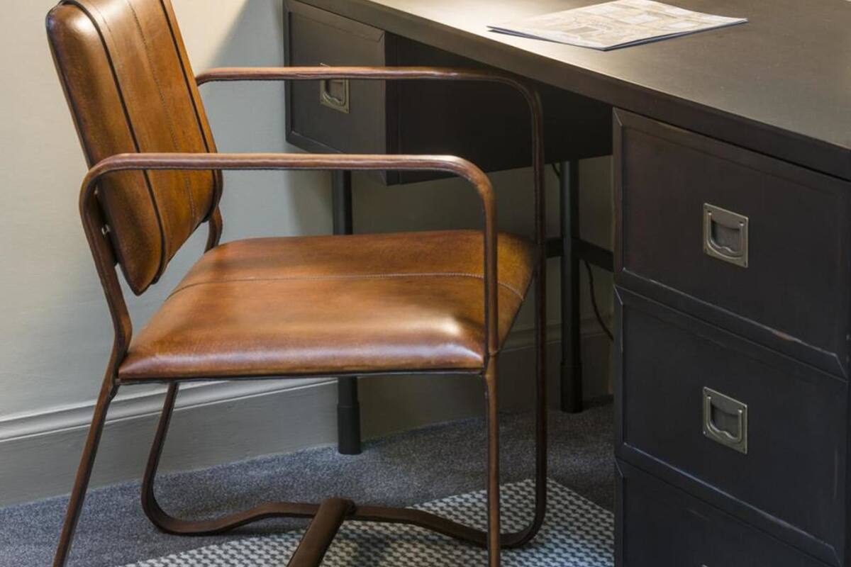 Een stoel met een houten rugleuning en zitvlak, geplaatst voor een donker bureau met lades.
