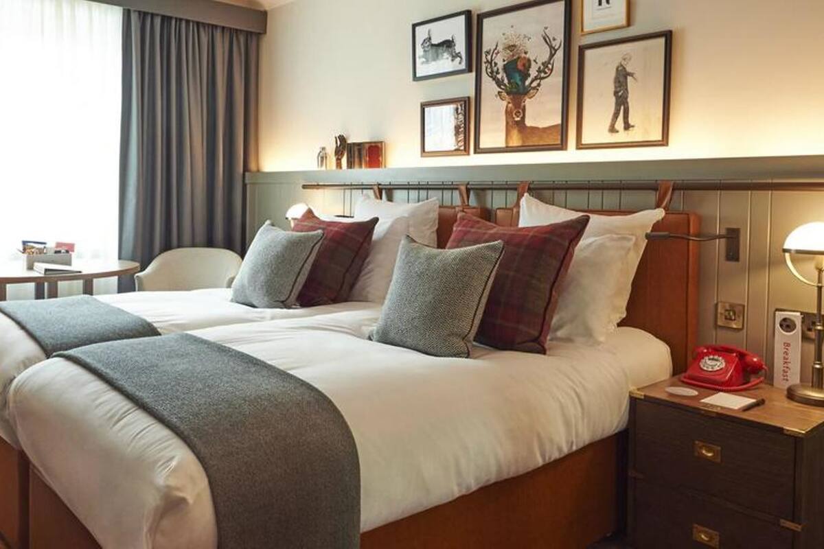 Een hotelkamer met een tweepersoonsbed, twee nachtkastjes, een stoel, een klein tafeltje en een lamp.