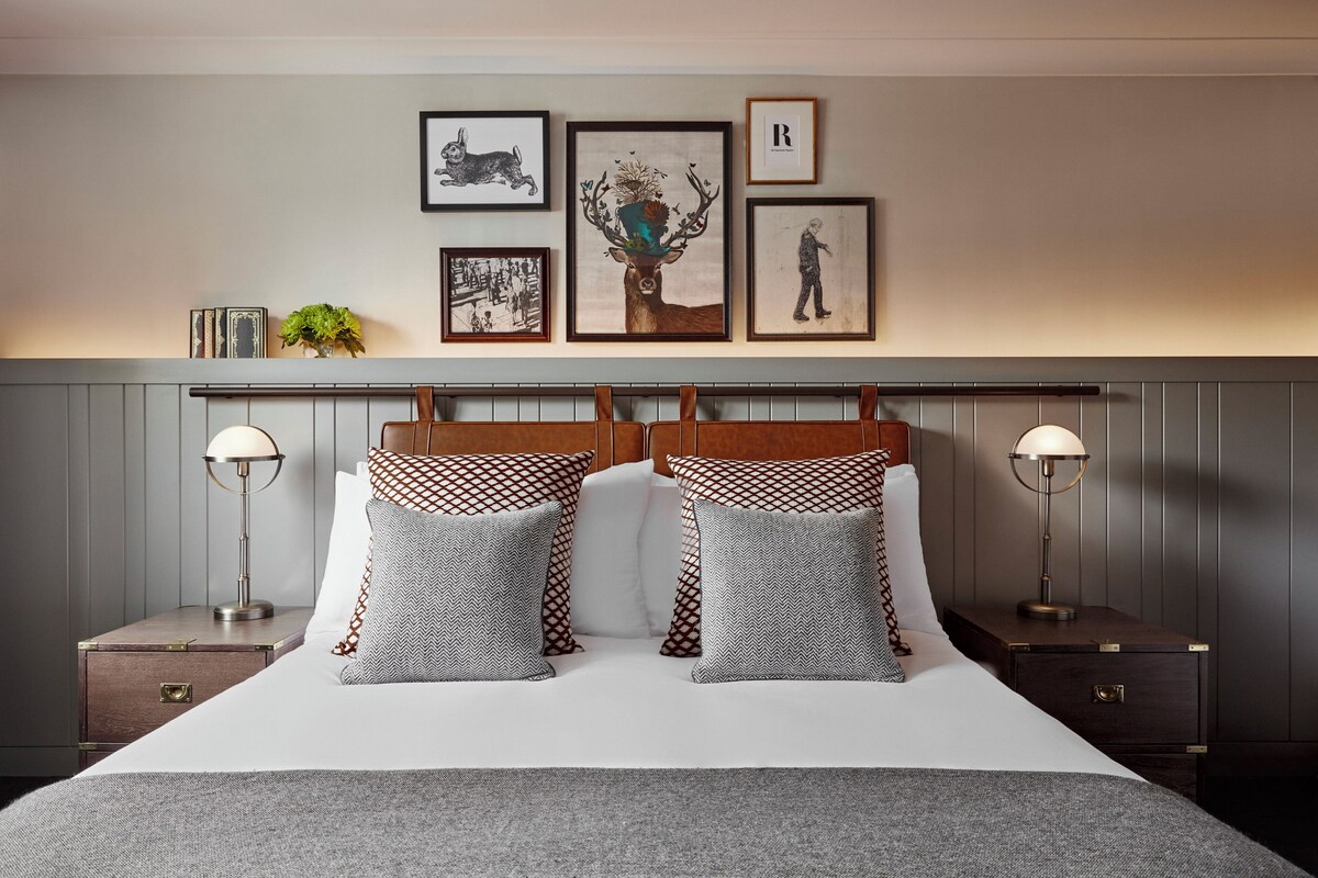 A neatly made bed with patterned pillows, a headboard with a decorative tree, and framed artwork on the wall.