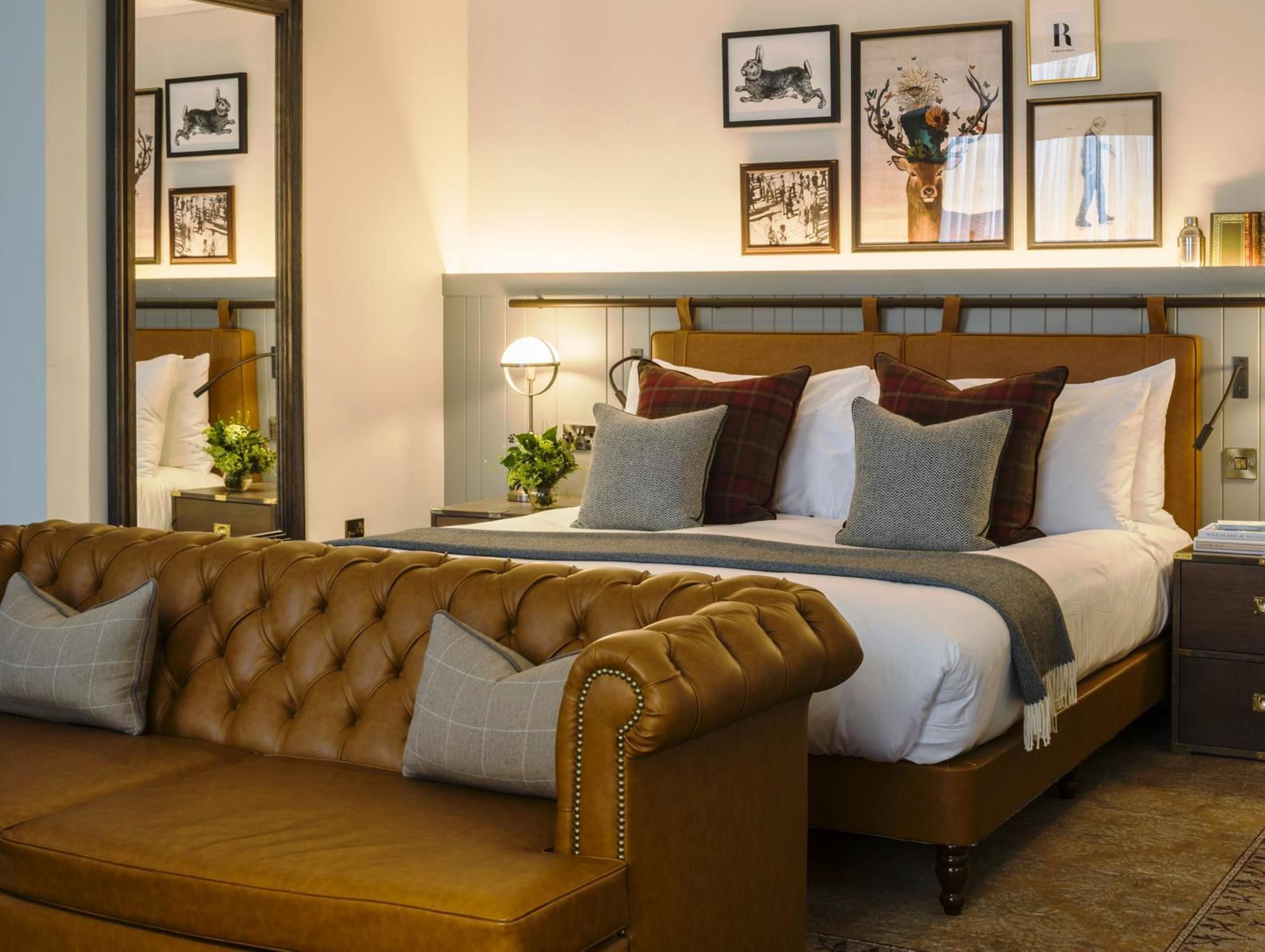 A hotel room with a large bed, a leather sofa, and framed artwork on the wall.