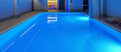 A large indoor swimming pool with a clear blue water surface, surrounded by walls with a tiled pattern.