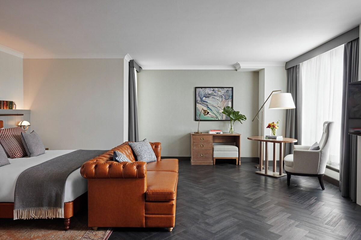 A modern hotel room with a large bed, a leather sofa, a desk, and a chair.