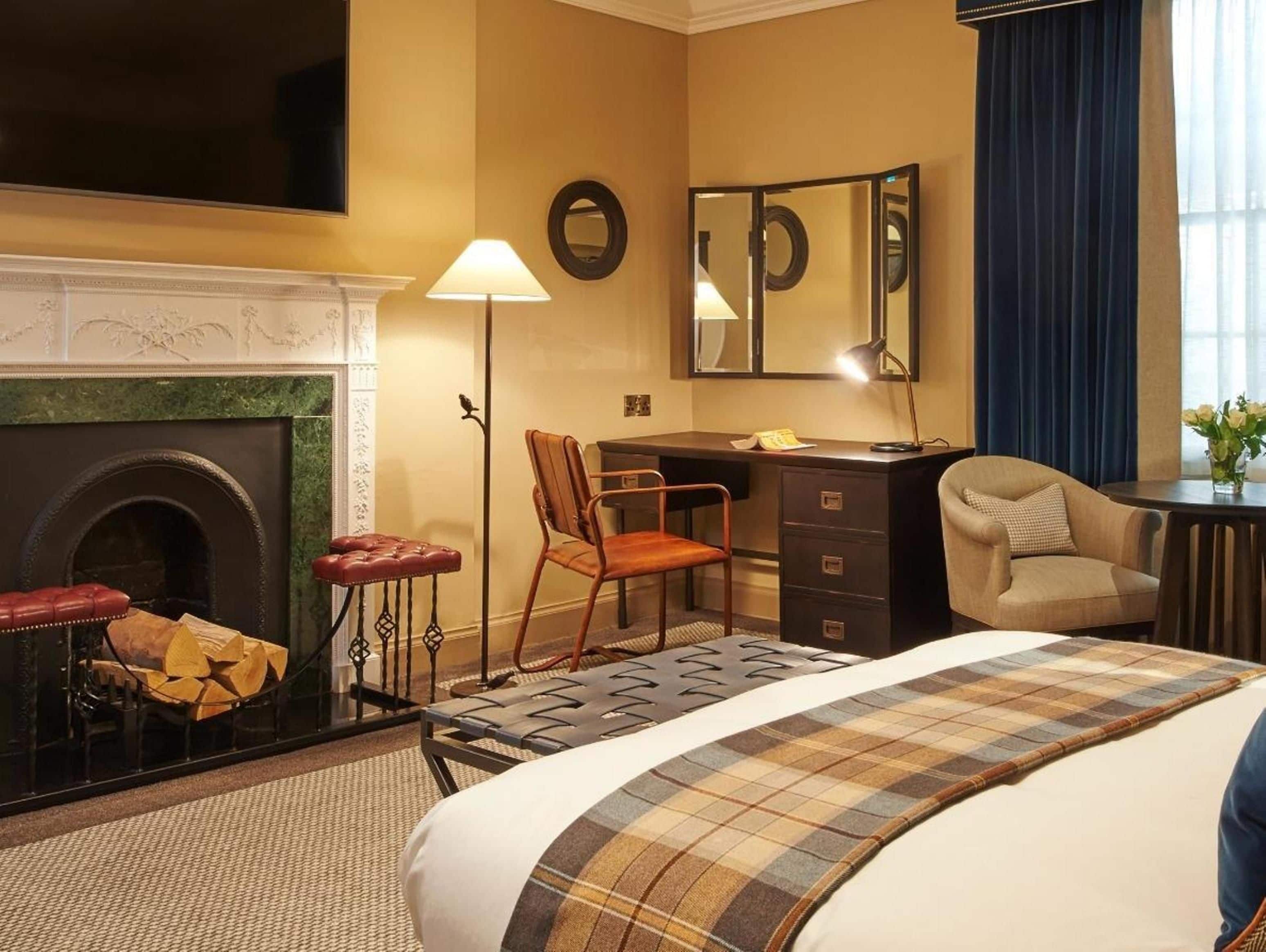 A hotel room with a fireplace, a desk, a chair, a bed, and a mirror.
