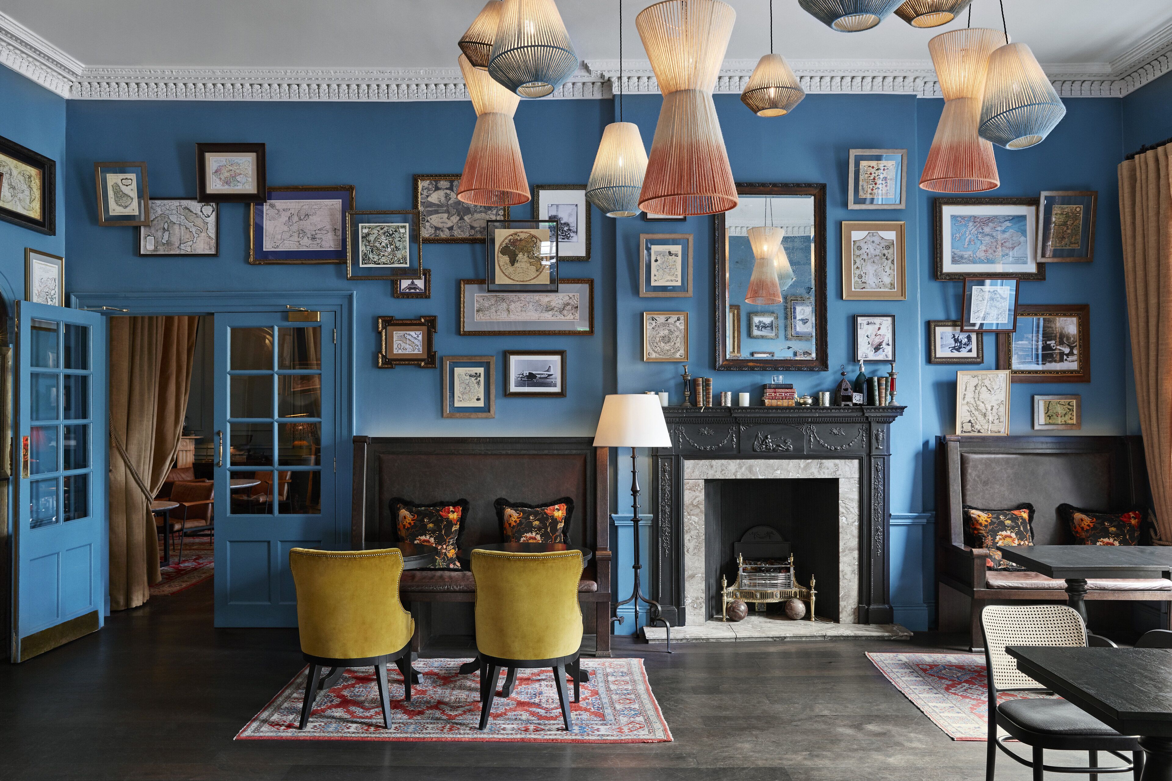 A room with a blue wall adorned with framed artwork, a fireplace, and a seating area with yellow chairs.