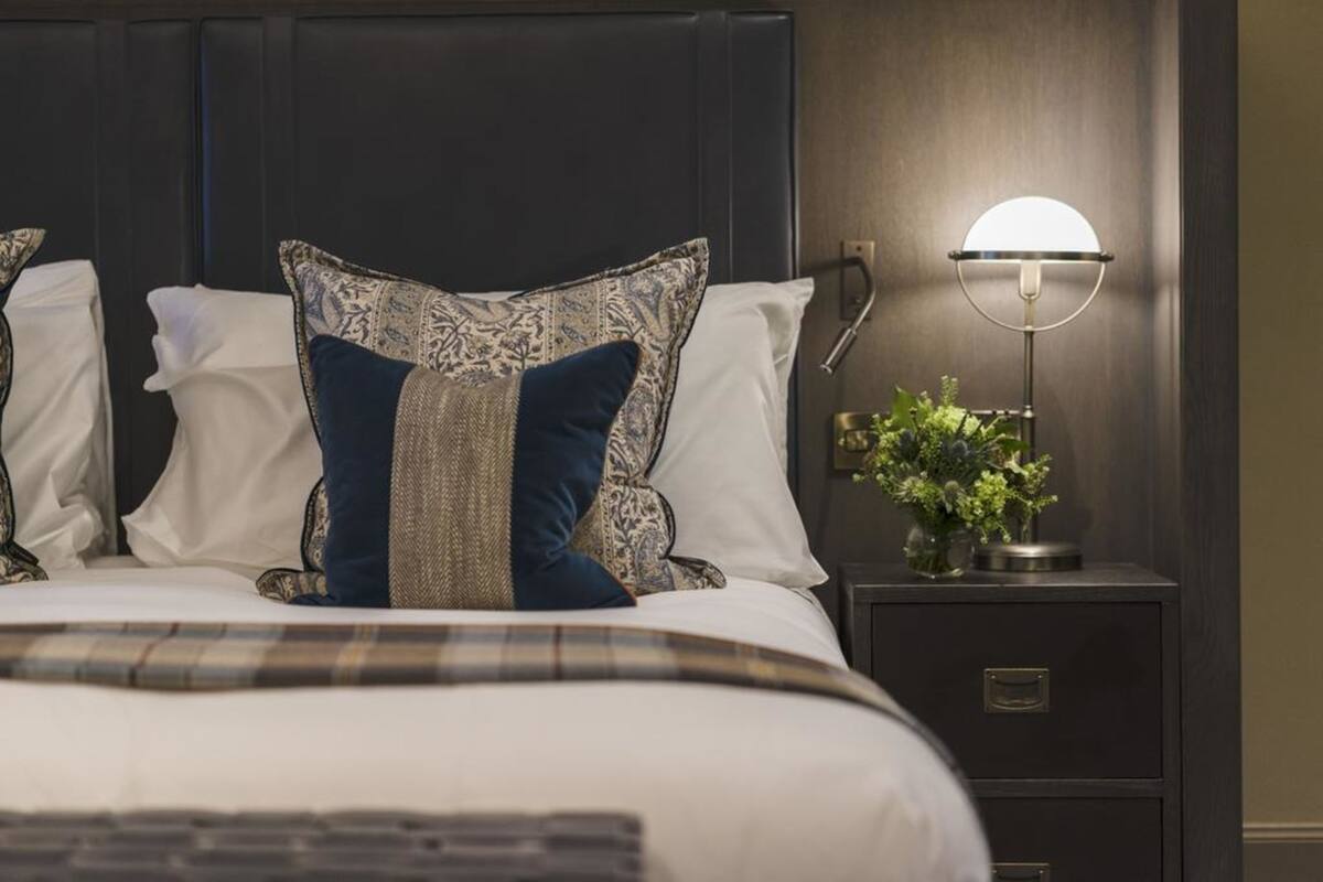 Een opgemaakt bed met gestreepte kussens, een bedlampje en een kleine plant op een nachtkastje.