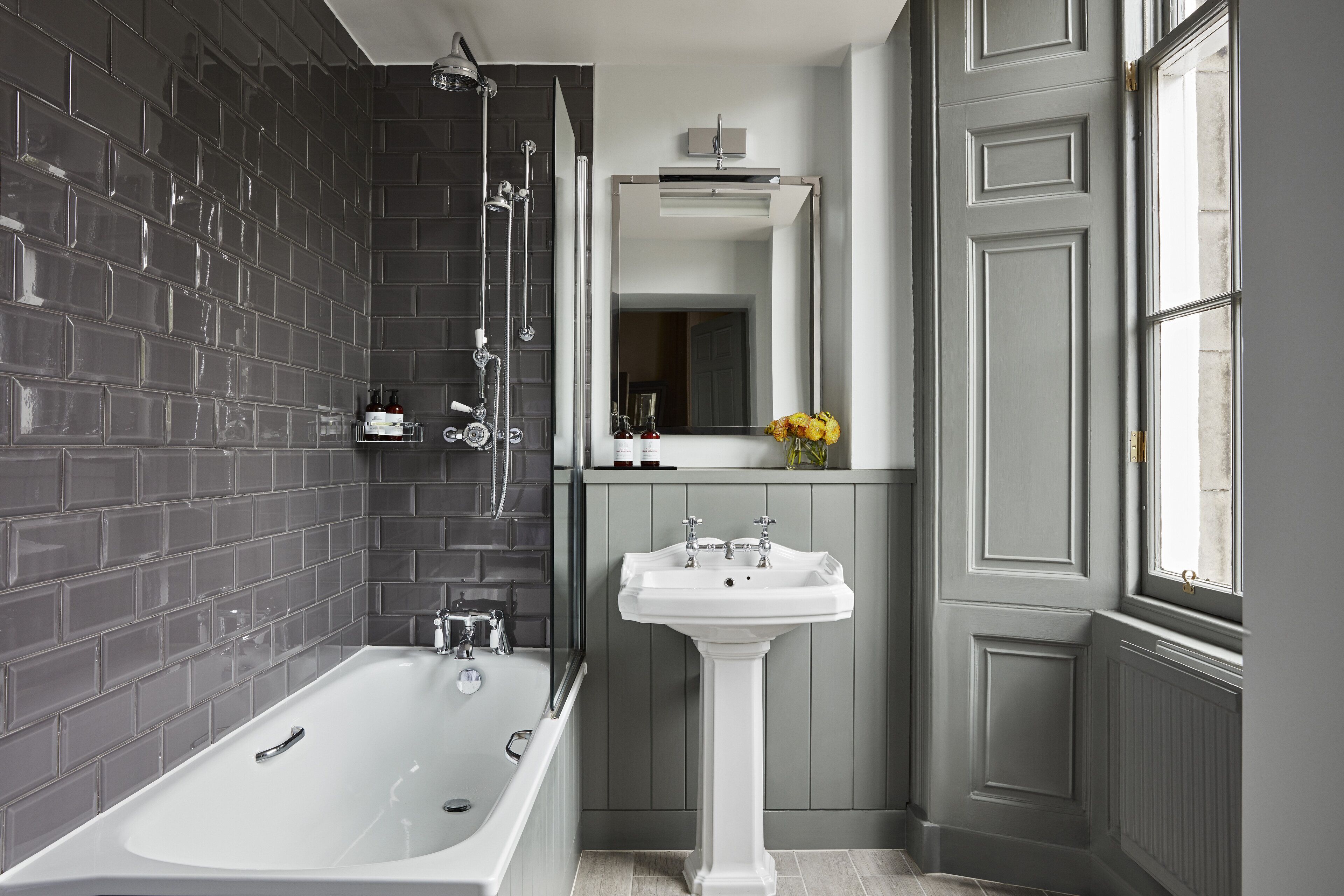 A modern bathroom with a bathtub, a pedestal sink, and a large mirror.