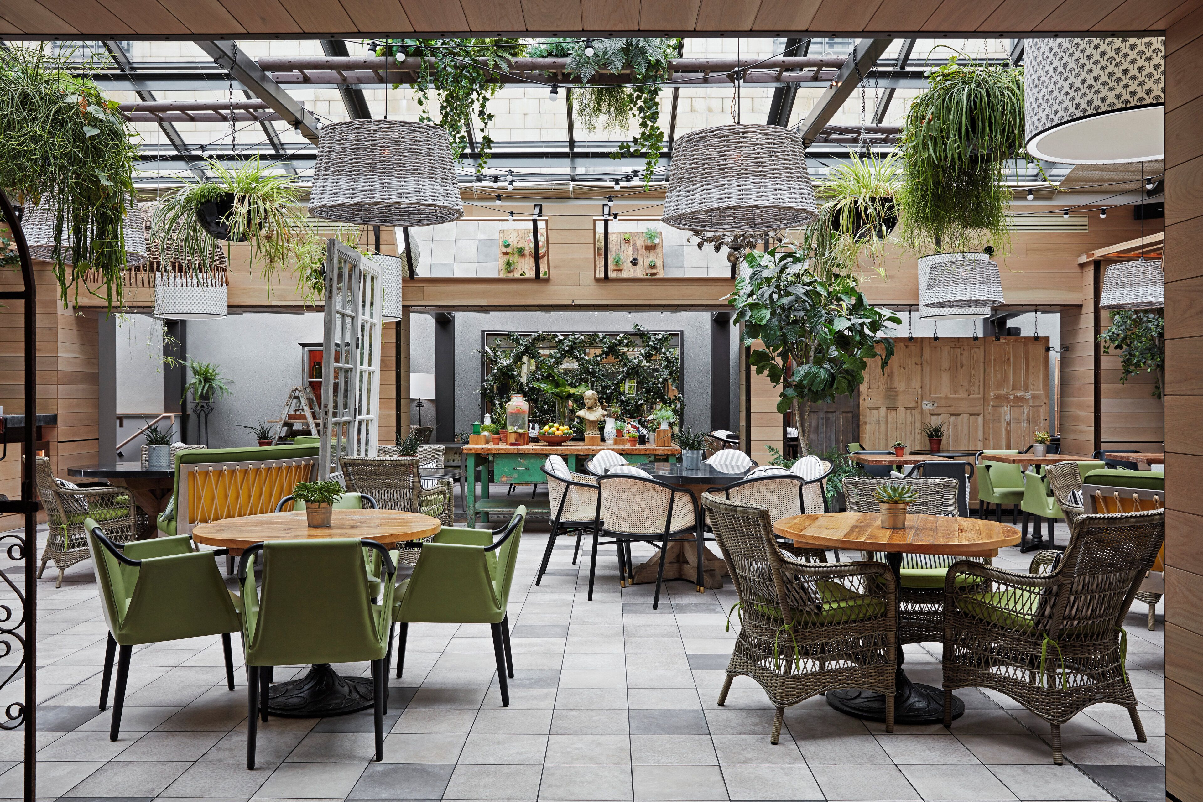 Un espace de restauration intérieur doté de nombreuses tables et chaises, agrémenté de plantes suspendues et offrant une vue sur le paysage urbain grâce à de grandes fenêtres.