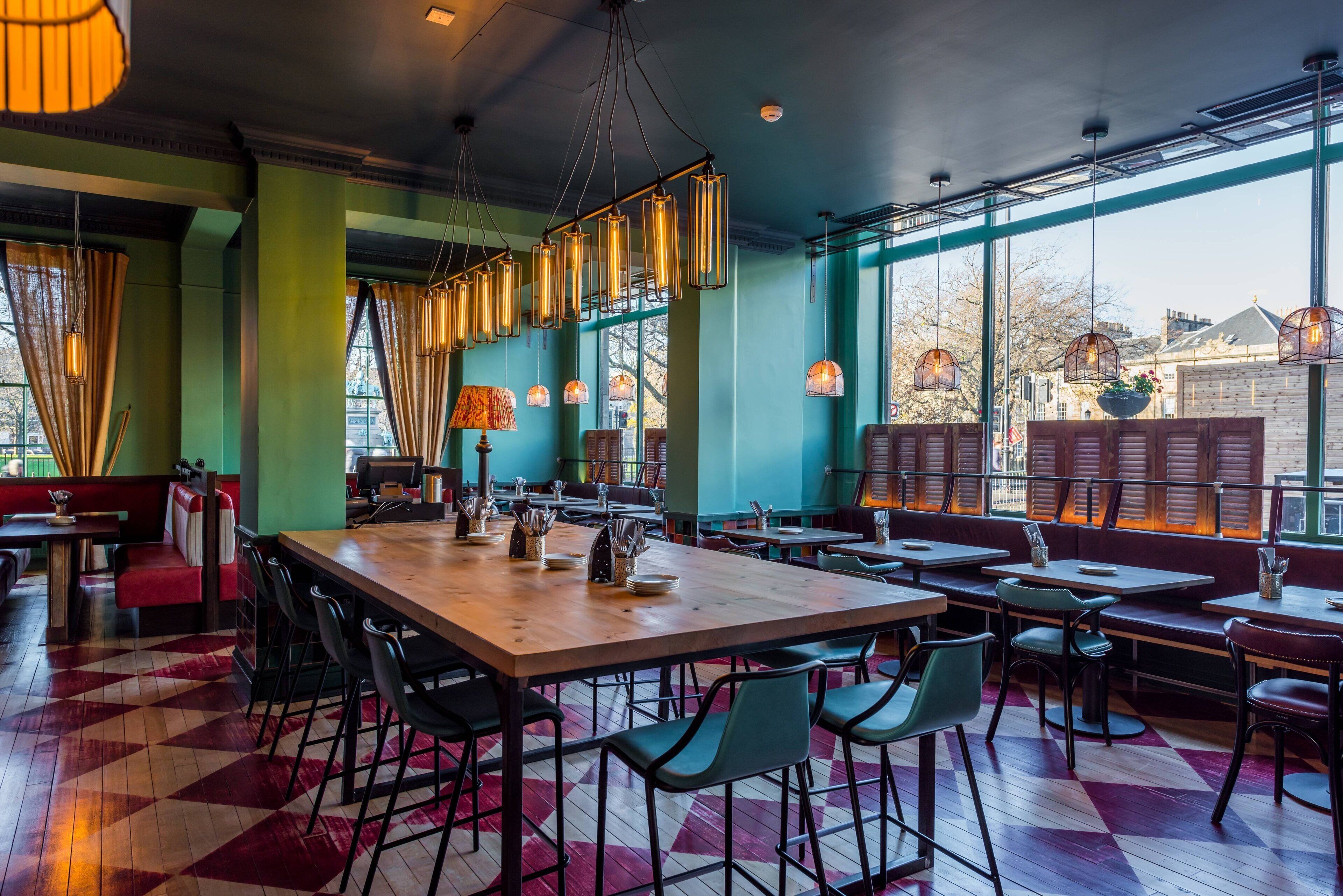 A restaurant with a large wooden table, green chairs, and a checkered floor pattern.