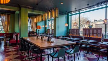 A restaurant with a large wooden table, green chairs, and a checkered floor pattern.