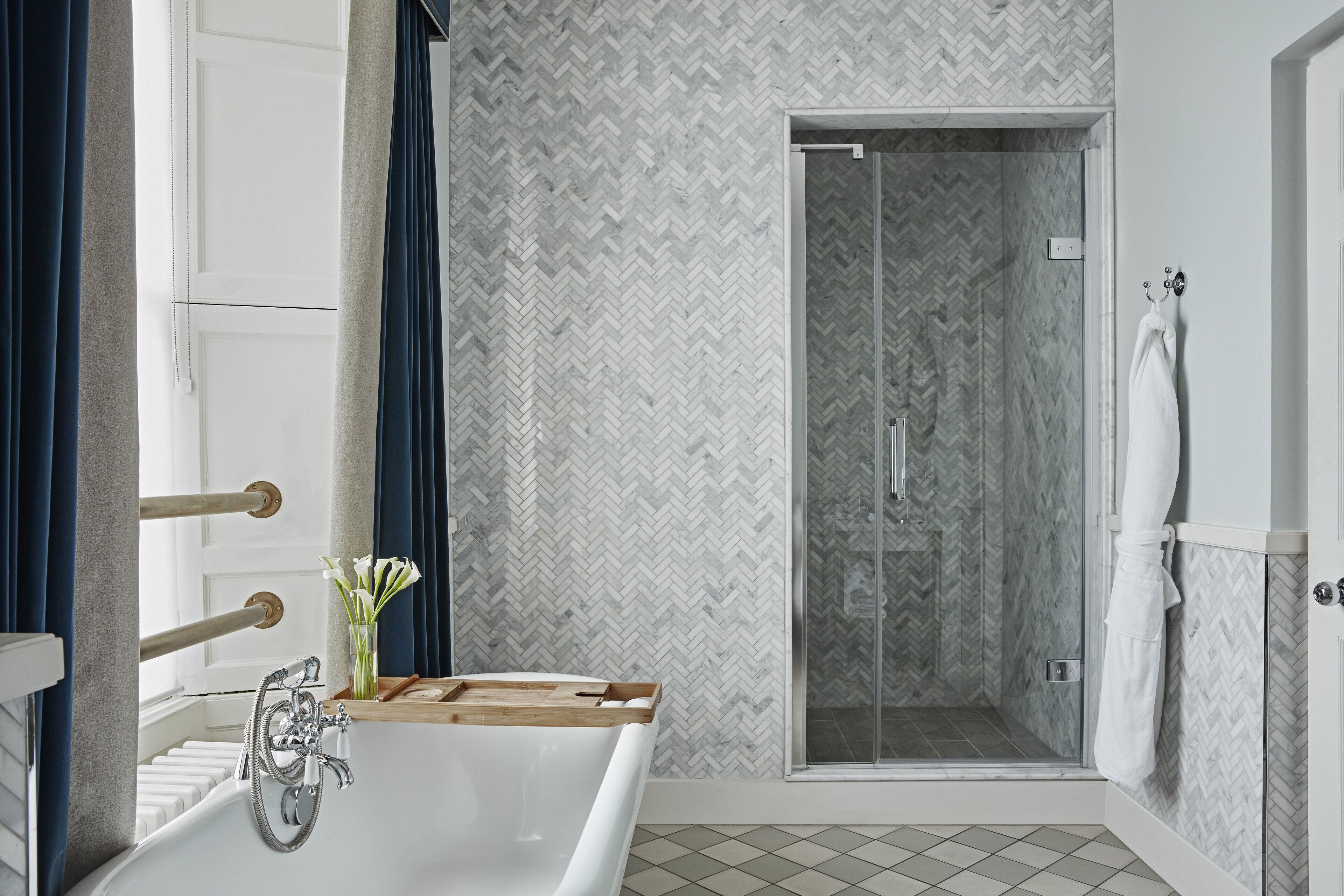Un bagno moderno con una vasca freestanding, una cabina doccia in vetro e una parete rivestita in piastrelle a motivi a spina di pesce.