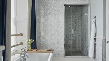 Une salle de bain moderne avec une baignoire sur pieds, une douche à parois de verre et un mur recouvert de carreaux disposés en motif chevrons.