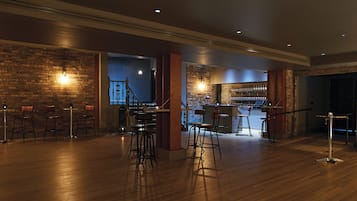 A spacious bar area with wooden flooring, brick walls, and multiple stools.