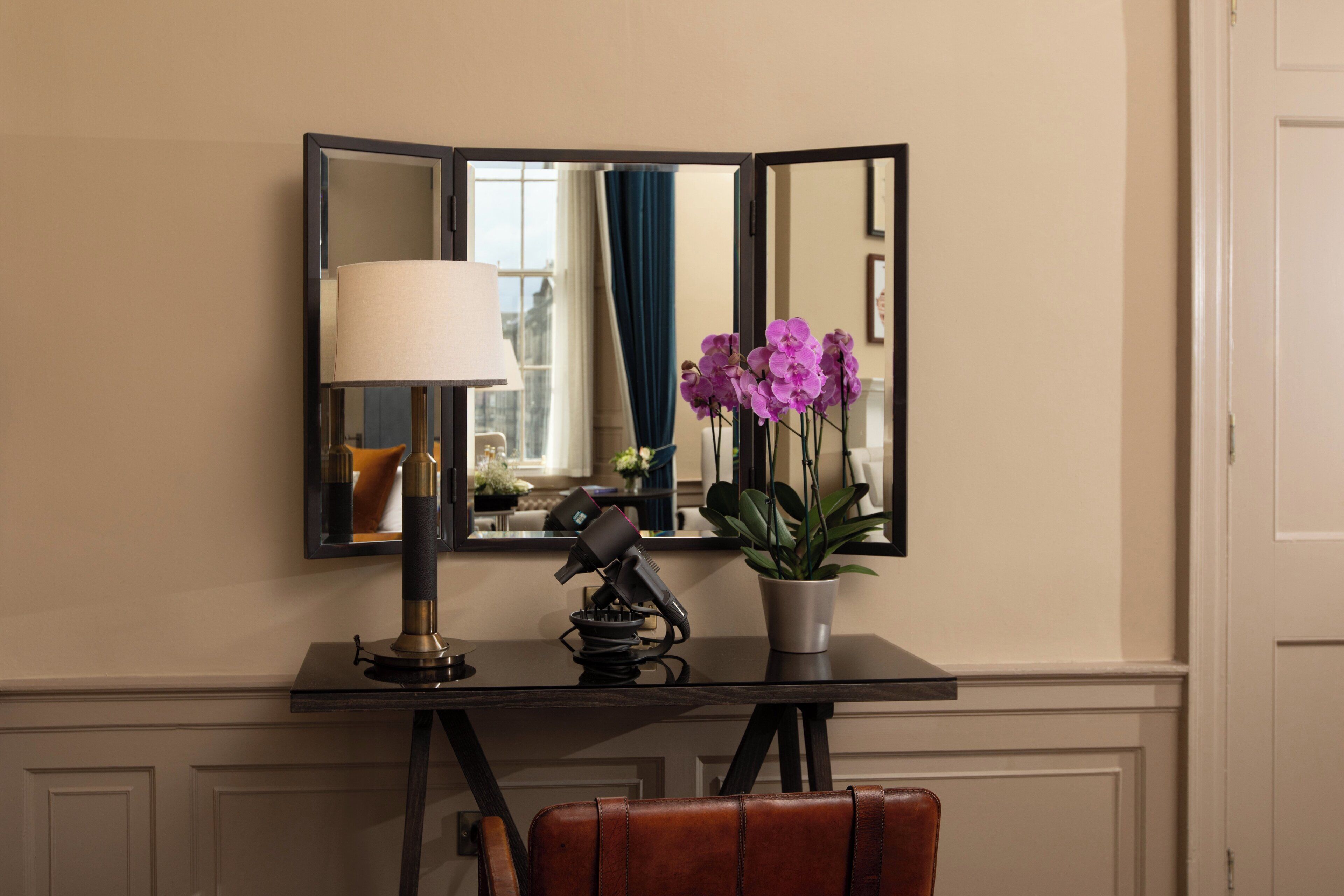 A room with a desk, a lamp, a mirror, a potted plant, and a chair.