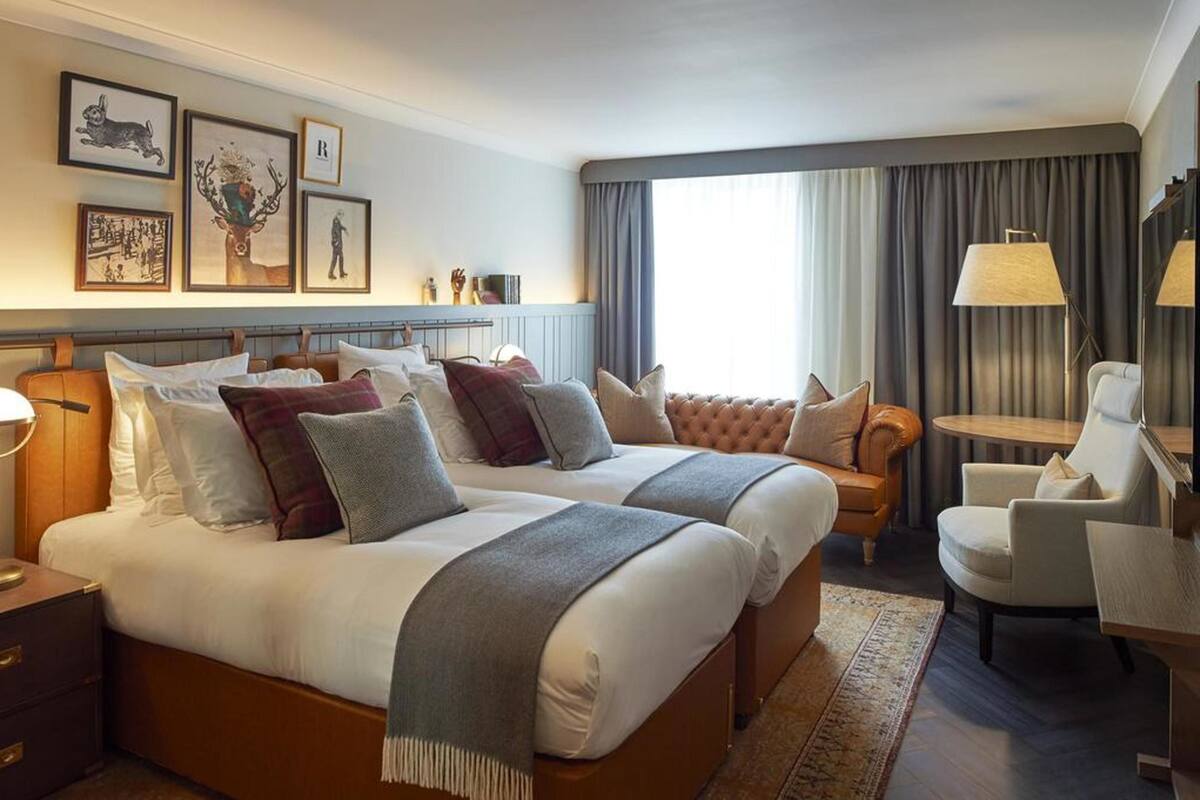 Een hotelkamer met twee bedden, een bureau, een stoel en een groot raam met gordijnen.