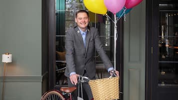 Un hombre con traje sostiene una bicicleta con una cesta y globos.