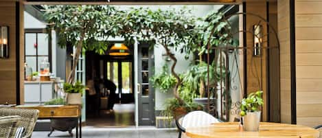 An indoor patio area with wicker furniture, a round wooden table, and potted plants.