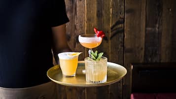 A person holding a tray with two drinks, one with a strawberry garnish and mint leaves, and another with an orange slice garnish.