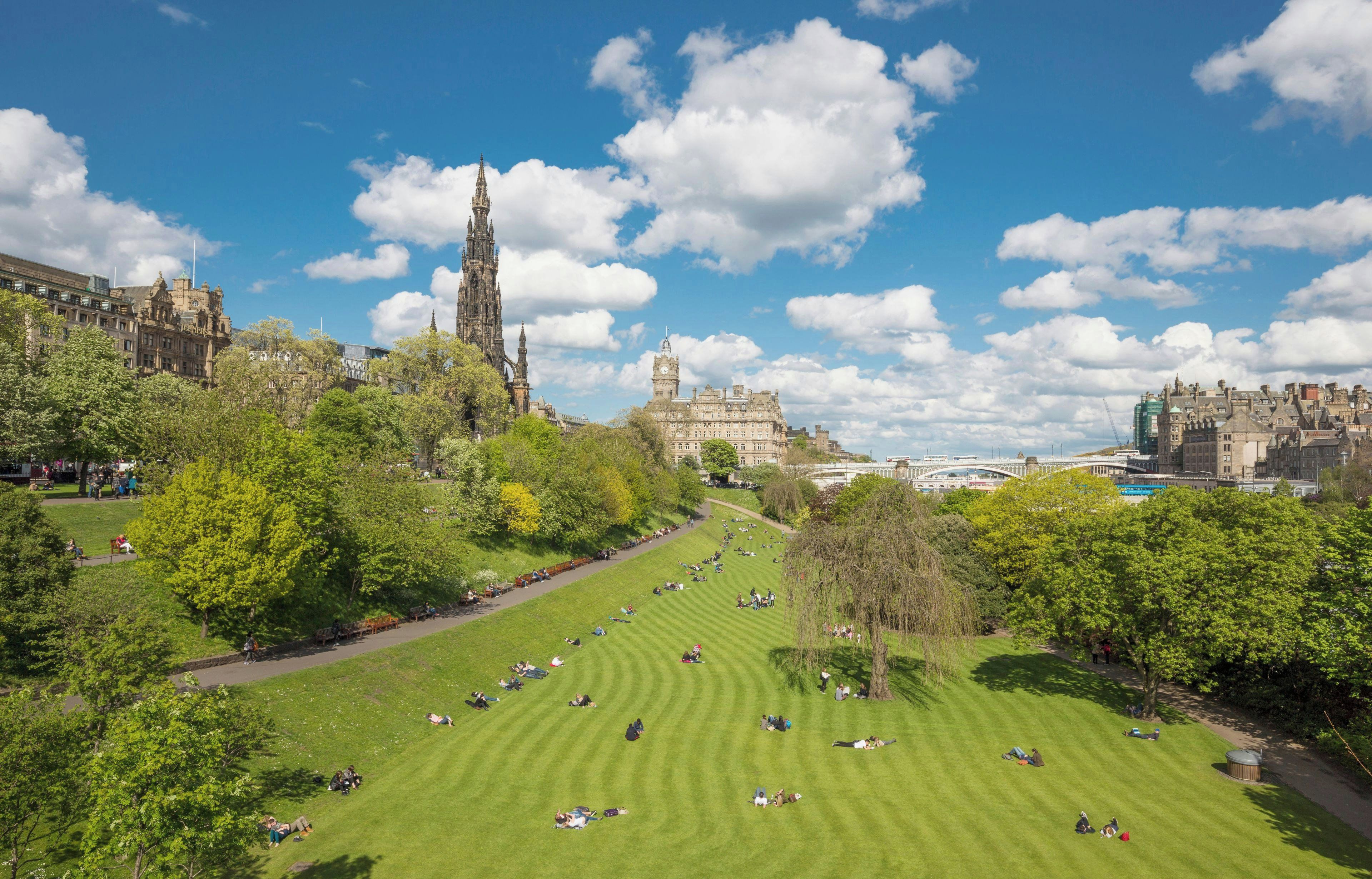 A park with a large lawn, a historic building, and a tower in the background.
