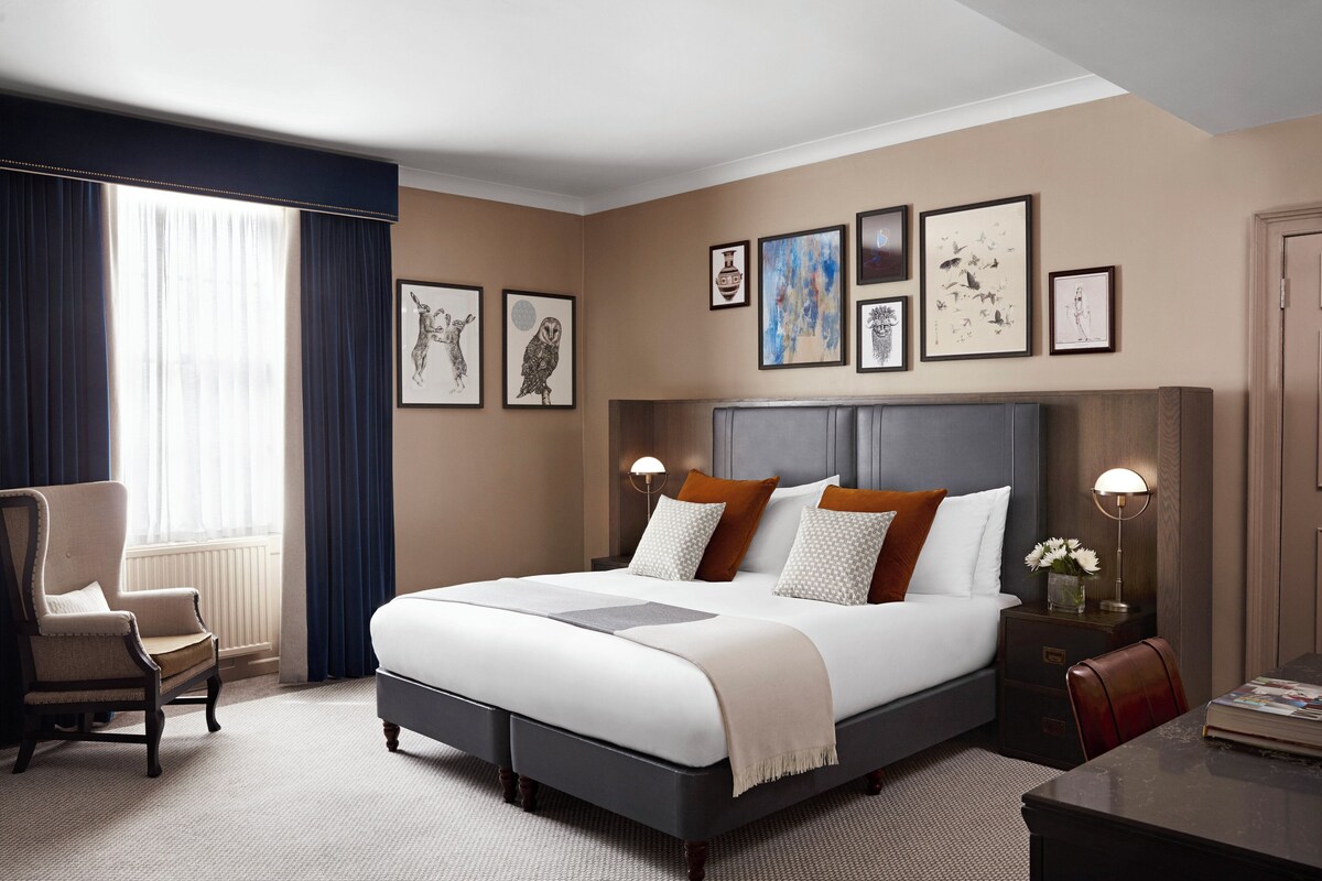 A neatly arranged hotel room with a large bed, a chair, a desk, and artwork on the walls.