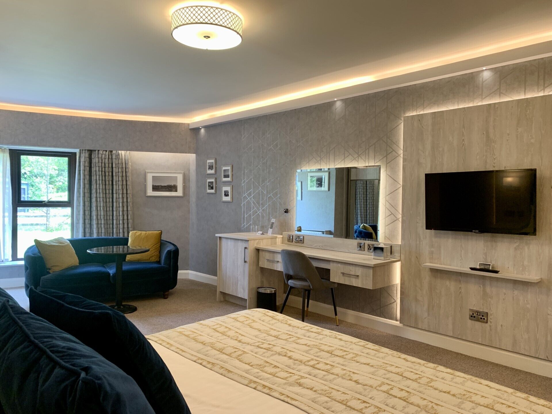 A modern hotel room with a bed, a desk, a television, and a window with curtains.