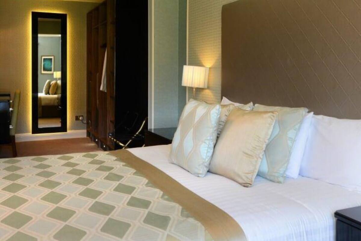 A hotel room with a large bed, a mirror, a nightstand, and a lamp.