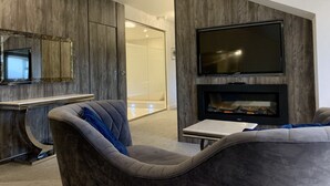 Ein modernes Wohnzimmer mit flachbildfernseher an der Wand, einem Kamin und einer Sitzecke mit Sofa und Sesseln.
