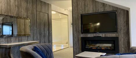 A modern living room with a flat-screen TV mounted on the wall, a fireplace, and a seating area with a sofa and armchairs.