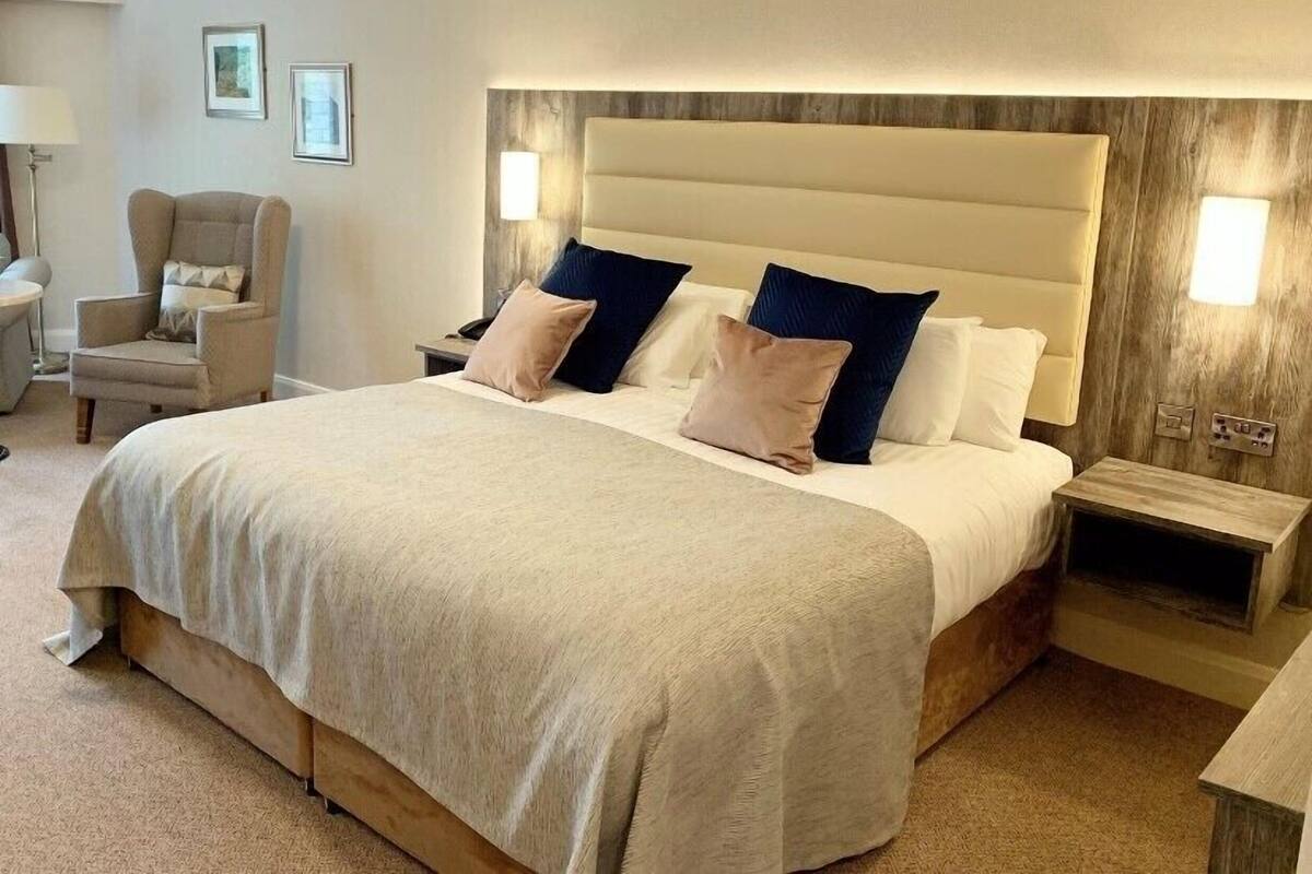 A hotel room with a large bed, two bedside tables, a chair, and a lamp.