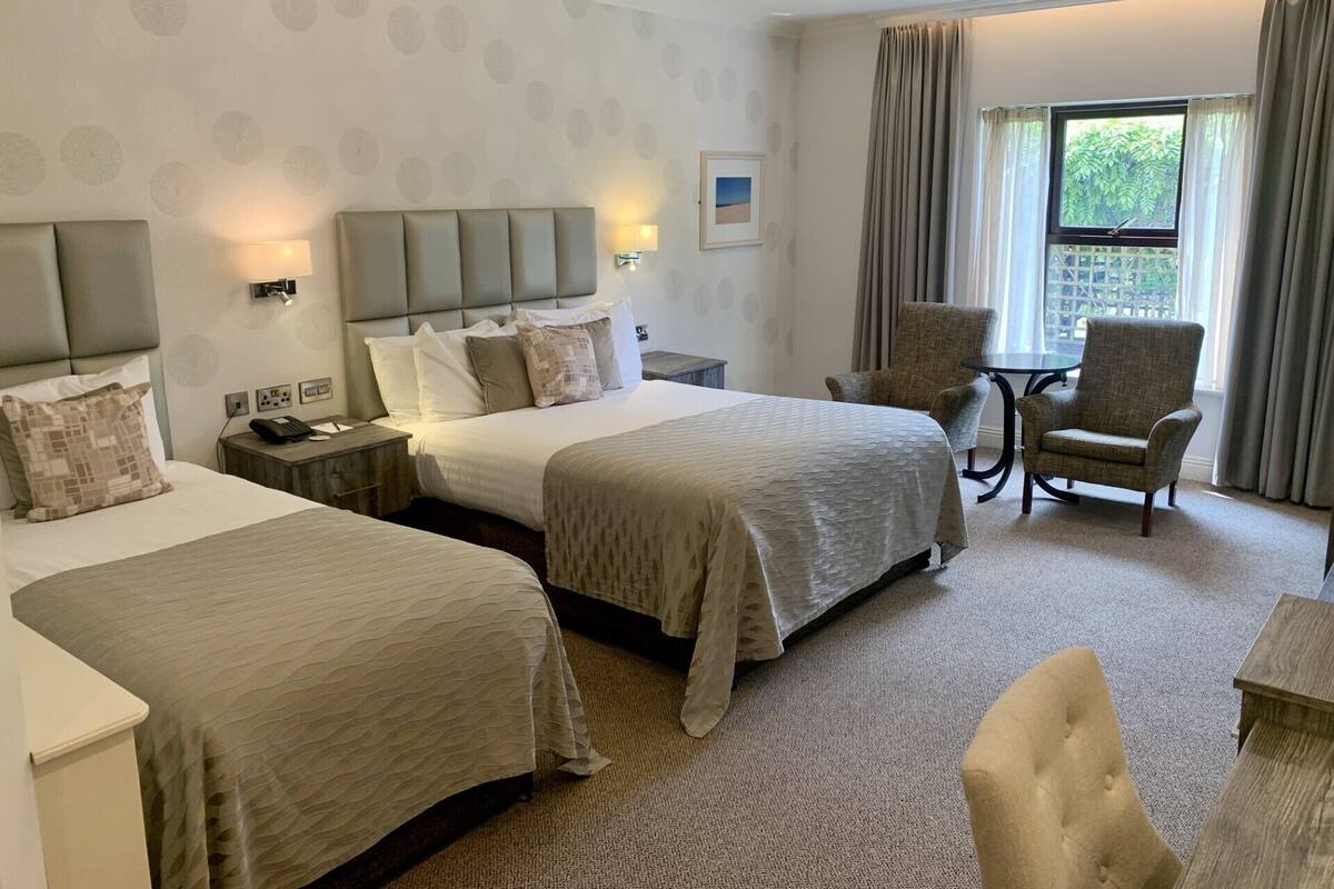 A hotel room with two beds, a chair, a table, and a window with curtains.