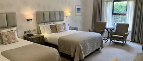 A hotel room with two beds, a chair, a table, and a window with curtains.