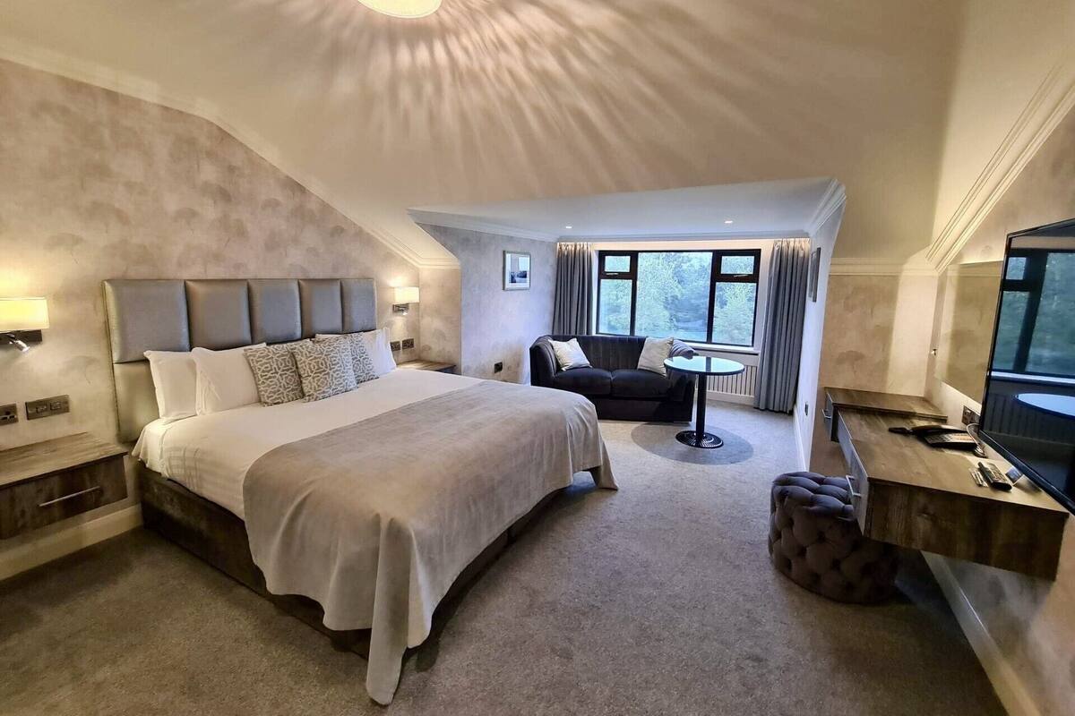 A modern hotel room with a large bed, a sofa, a desk, and a TV.