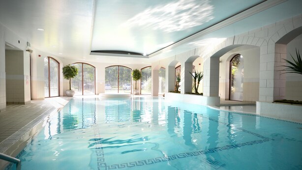 Ein großer, überdachter Swimmingpool mit klarem Wasser, umgeben von Bogenfenstern und Topfpflanzen.