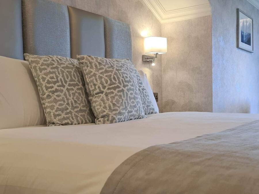 Un dormitorio con una cama grande, almohadas estampadas, una lámpara de pared y un cuadro en la pared.