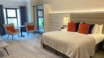Une chambre d’hôtel avec un grand lit, deux chaises, une petite table et une table de chevet avec un téléphone.