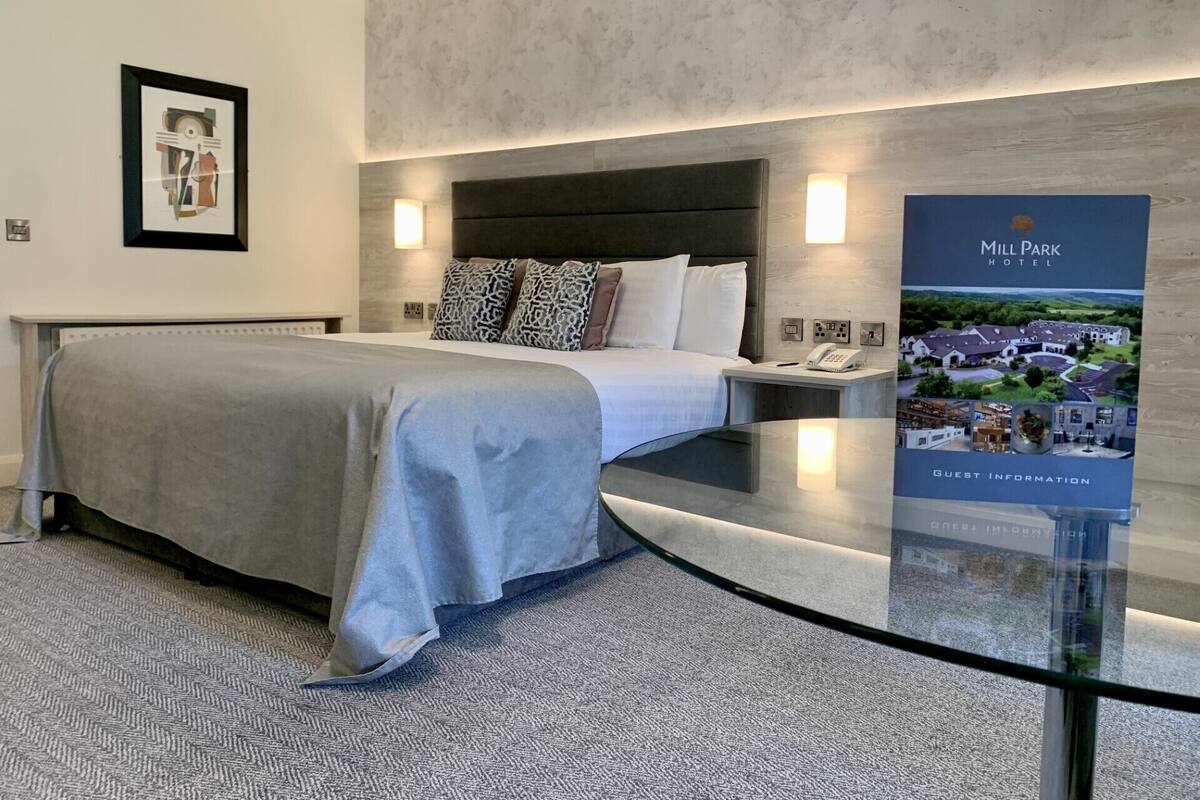 A modern hotel room with a bed, bedside table, and a poster of Mill Park Hotel.