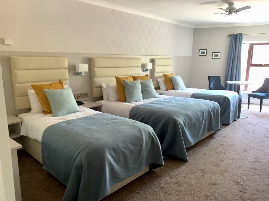 Une chambre d’hôtel avec trois lits, chacun doté d’une tête de lit, et une petite table avec des chaises.