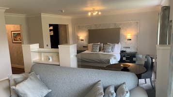 Ein modernes Hotelzimmer mit einem großen Bett, einer Couch, einem Esstisch und einer kleinen Küchenzeile.